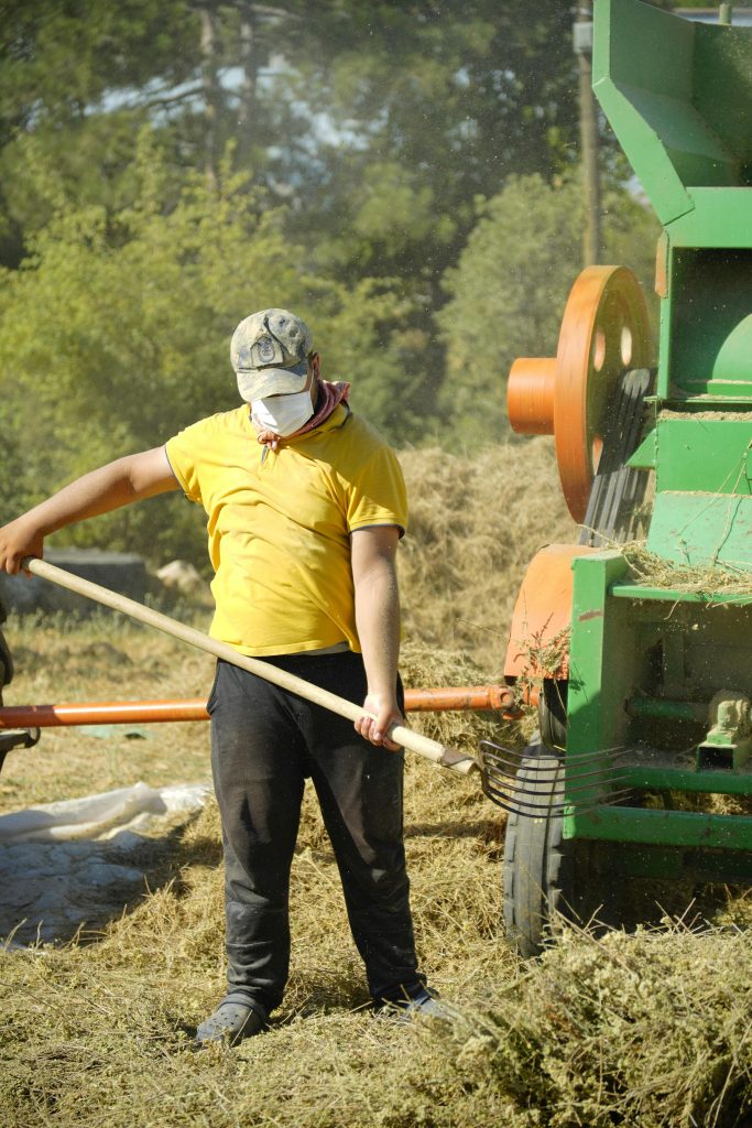 Man operates hay baler amidst hay piles under sunny skies in Türkiye's countryside.